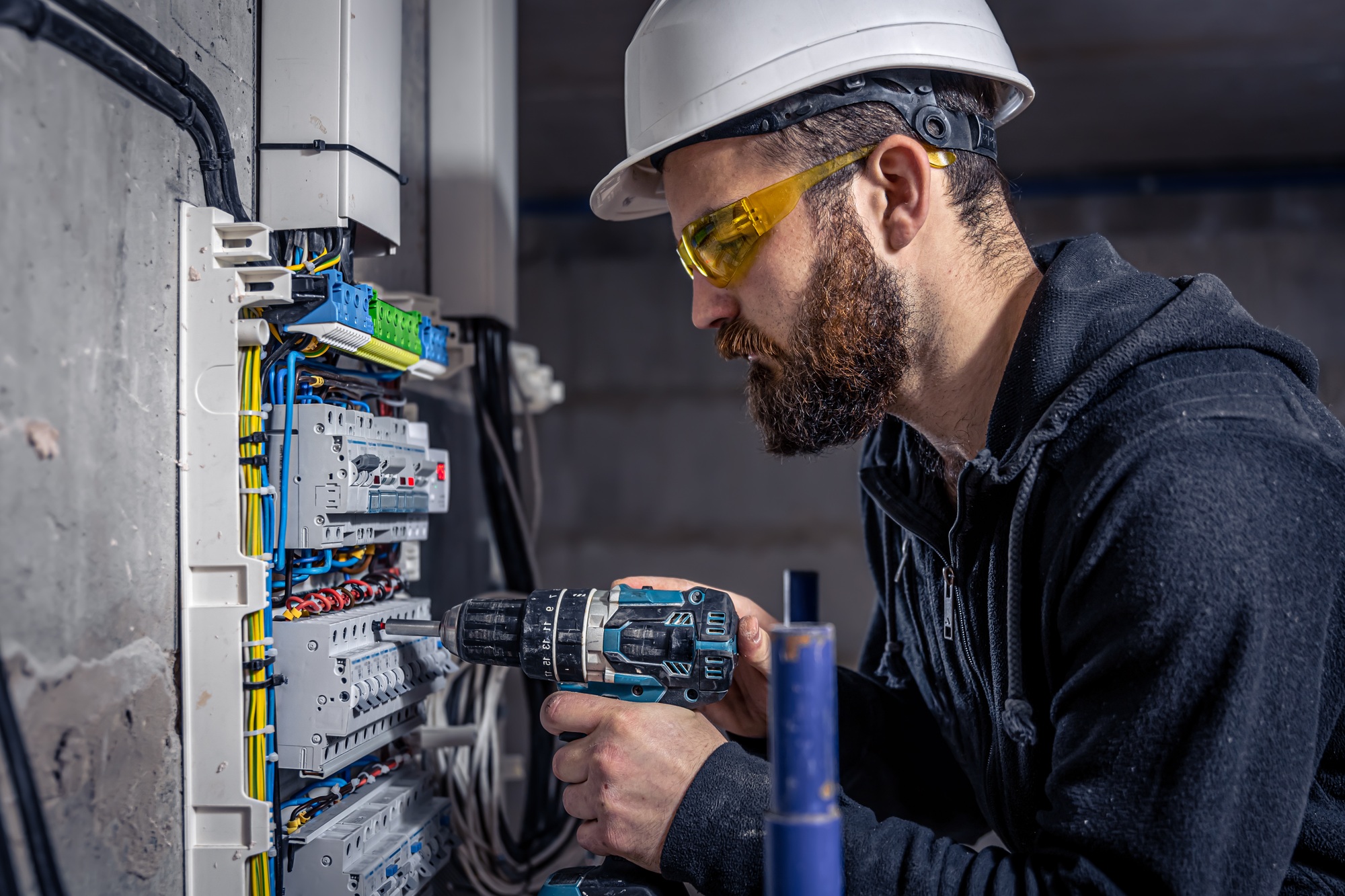 A male electrician works in a switchboard with an electrical connecting cable.