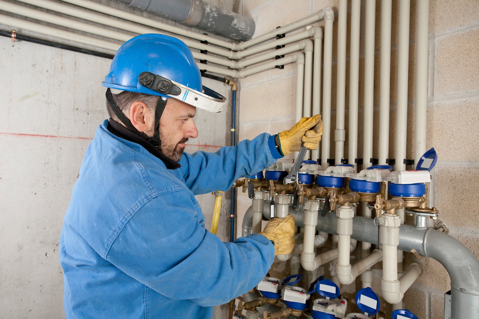 A technician works on plumbing valves in a utility room during the day